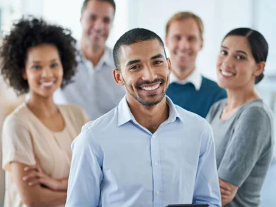 Imagem de um homem sorrindo a frente de sua equipe com pessoas de diferentes etnias